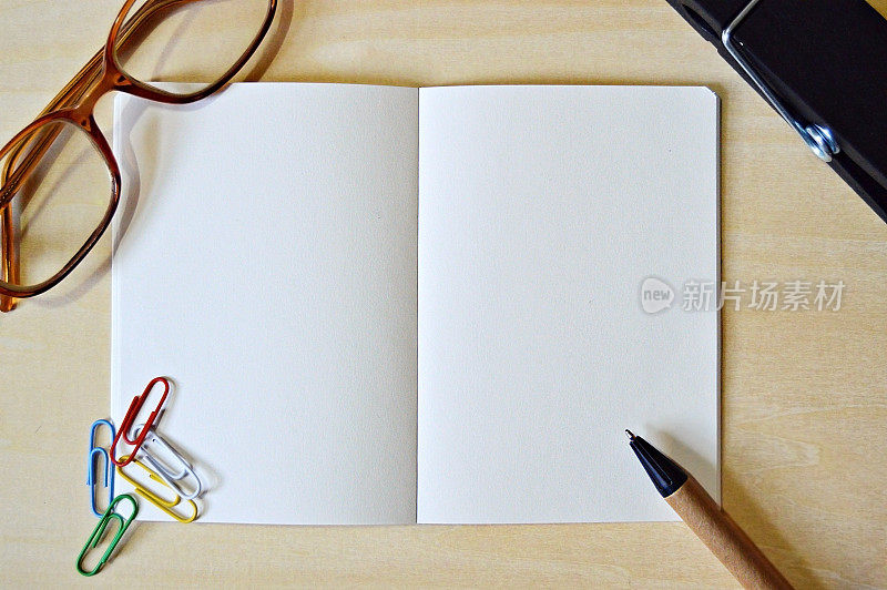 一张水平的照片，一张白色的素色记事本，一个棕色和黑色的钢笔和彩色回形针，眼镜放在一个木制的米色水平背景上，很有美感。