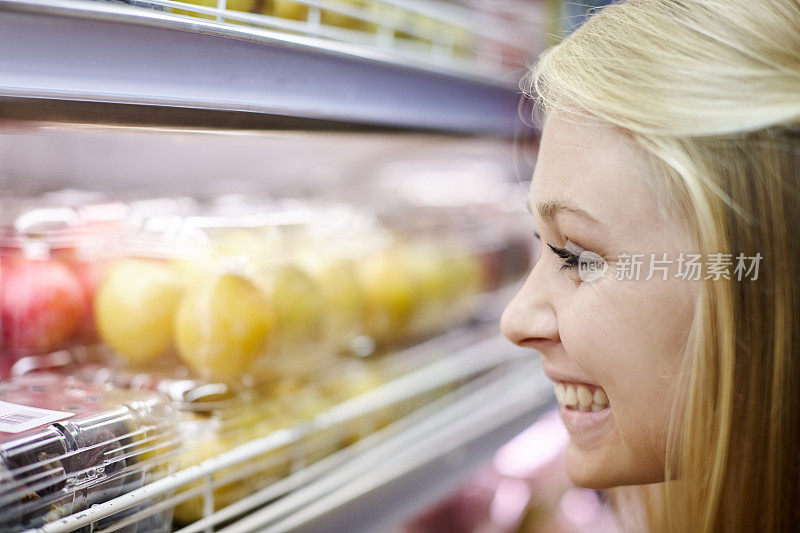 漂亮的金发美女在超市冰箱里挑选水果