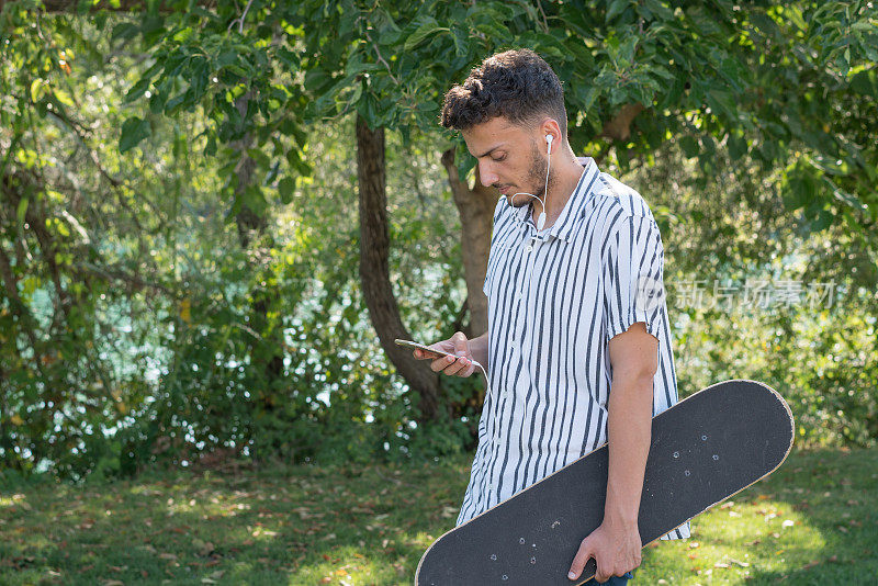 玩滑板的人在大自然中行走，用智能手机听音乐