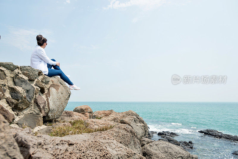 坐在海滩边岩石上的女人