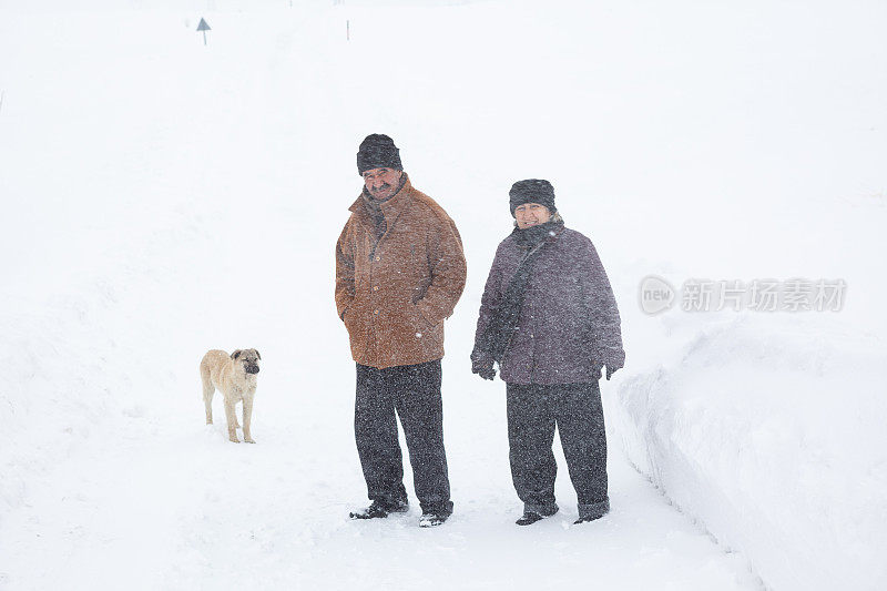 一对老年夫妇在下雪的乡村路上穿着暖和的衣服