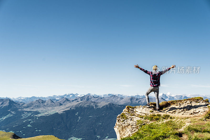 一个人站在岩石的边缘，举起双手。靠近塞塞达的意大利阿尔卑斯山。