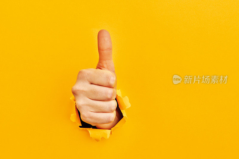 人的手从撕破的黄色纸中伸出来，竖起大拇指