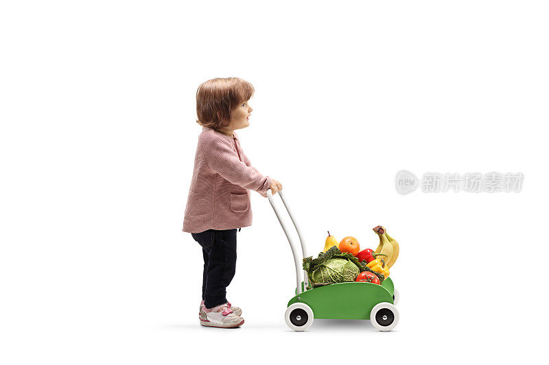 小女孩推着一辆装着水果和蔬菜的玩具车