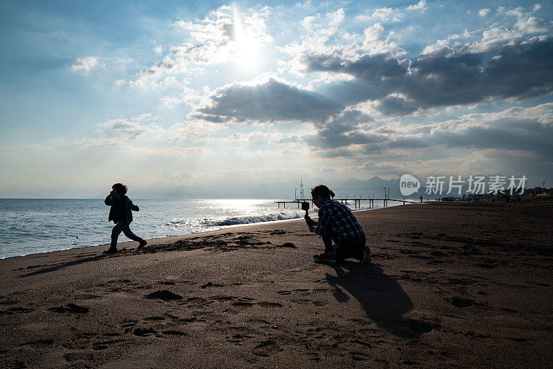 年轻女子用智能手机在海滩上拍摄男孩