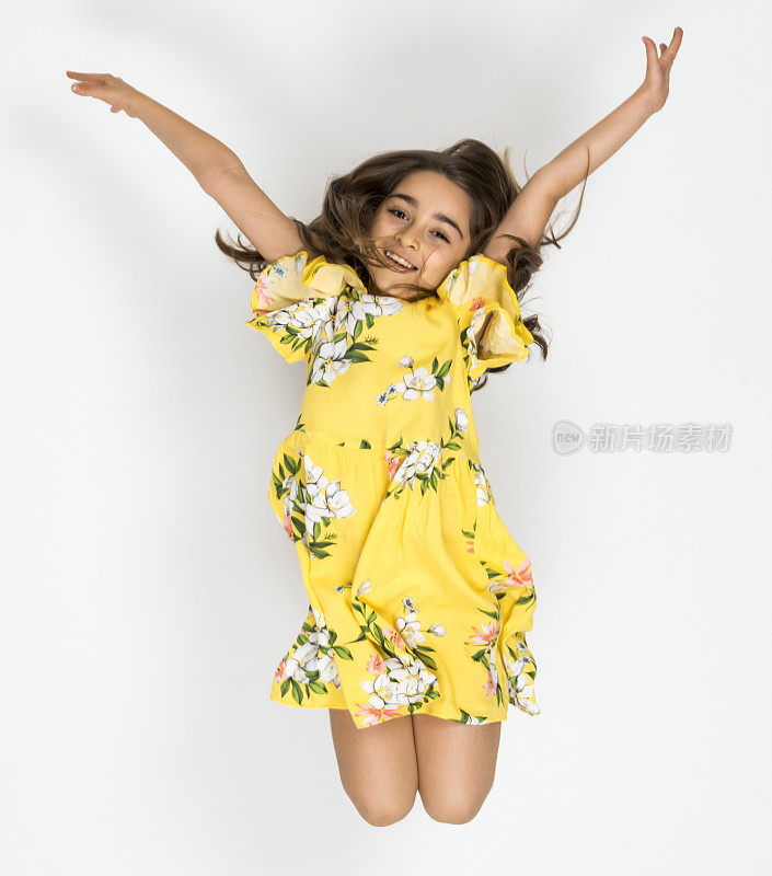 一个漂亮的小女孩的肖像微笑和跳跃的手臂在空中举起白色的背景