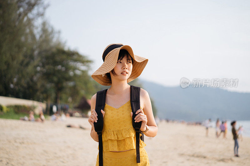 年轻的亚洲女游客与沙滩帽走在海滩上