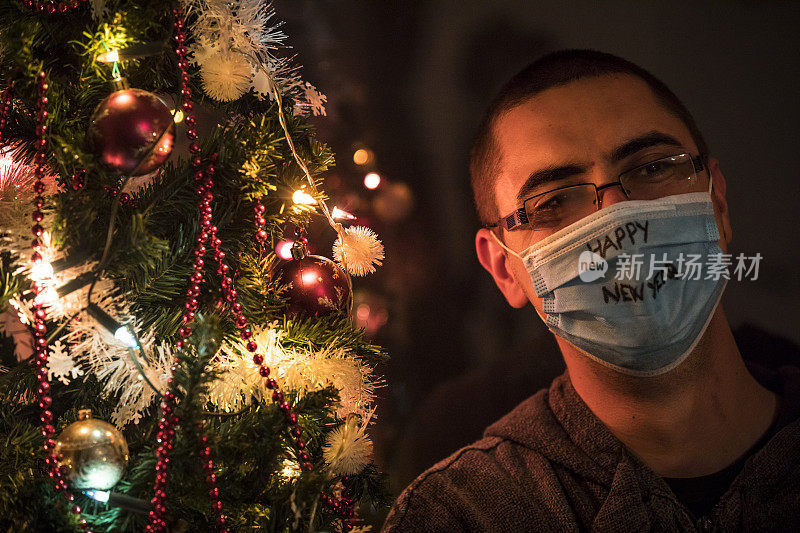 一名年轻人戴着防护面具，在圣诞树旁说“新年快乐”