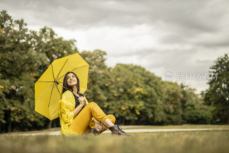 美丽的年轻女子穿着黄色雨衣，拿着黄色雨伞在户外