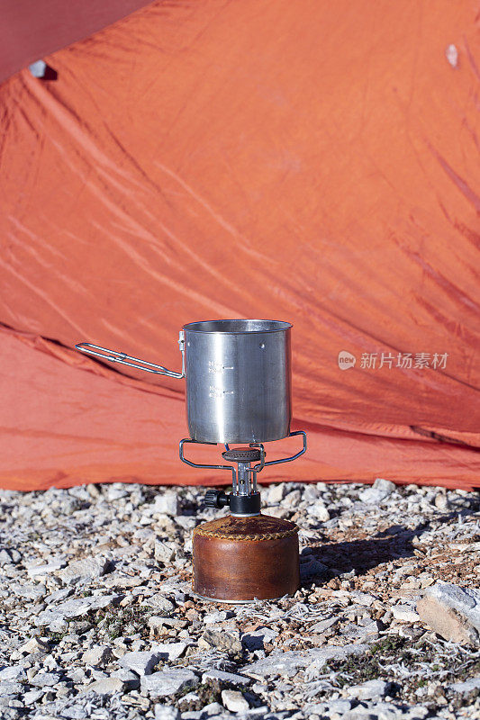 在徒步旅行期间的帐篷背景上，带有现代钛锅的燃气弹野营喷气炉