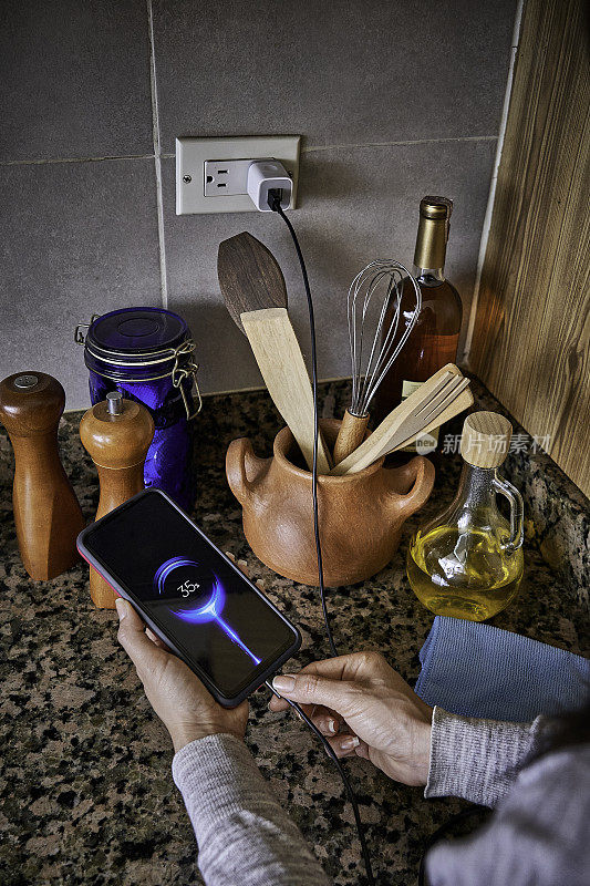 一名年轻女子在家中厨房里用手将充电电缆连接到智能手机上