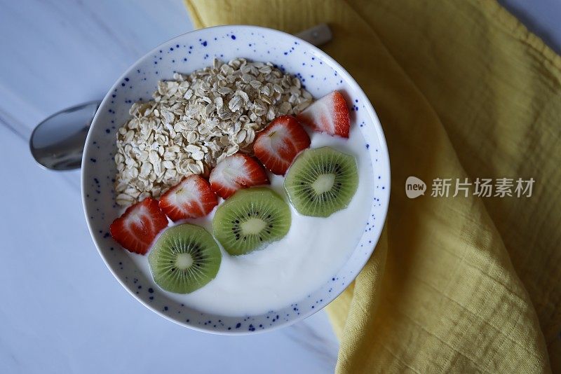 健康早餐，碗里装饰着草莓片和猕猴桃燕麦酸奶，背景是灰白色大理石，社交媒体趋势早餐，特写