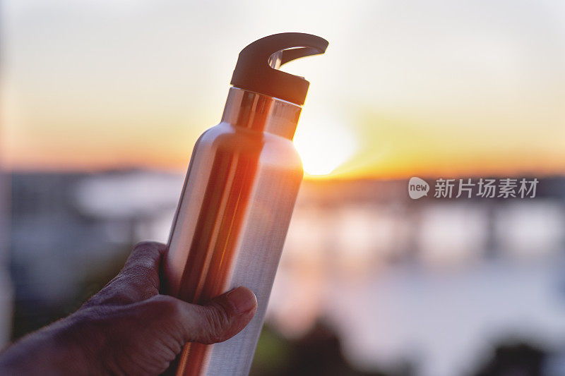日落时分，一名男子举着一个可重复使用的金属水瓶。