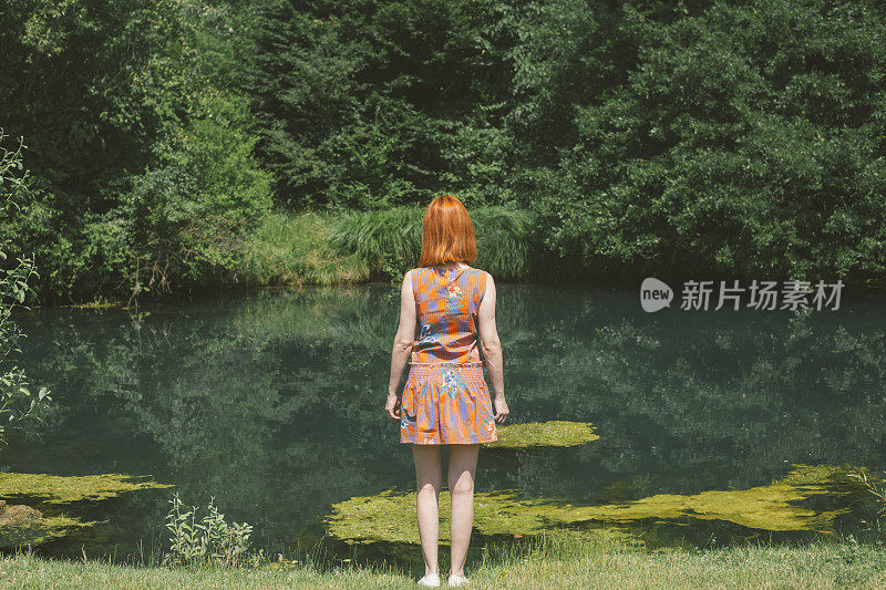 红头发瘦弱的女孩旁边的一个小池塘