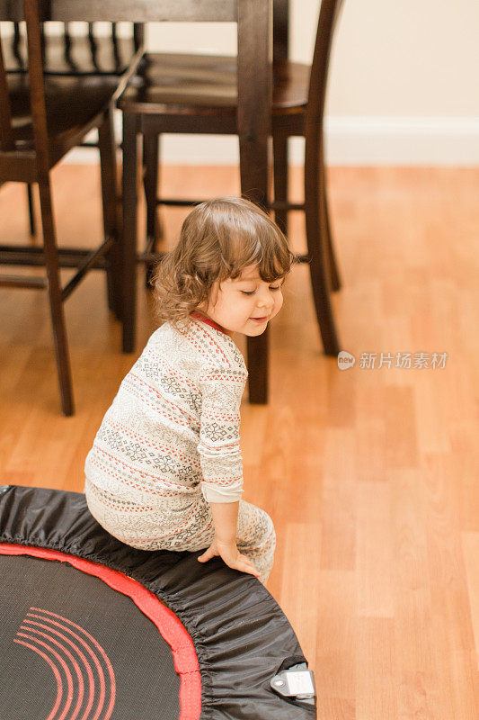 2019冠状病毒病期间，两岁女童坐在黑色和红色蹦床上进行家庭玩耍和学习