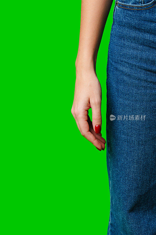 一个女人侧身站在绿色背景下，穿着牛仔牛仔裤