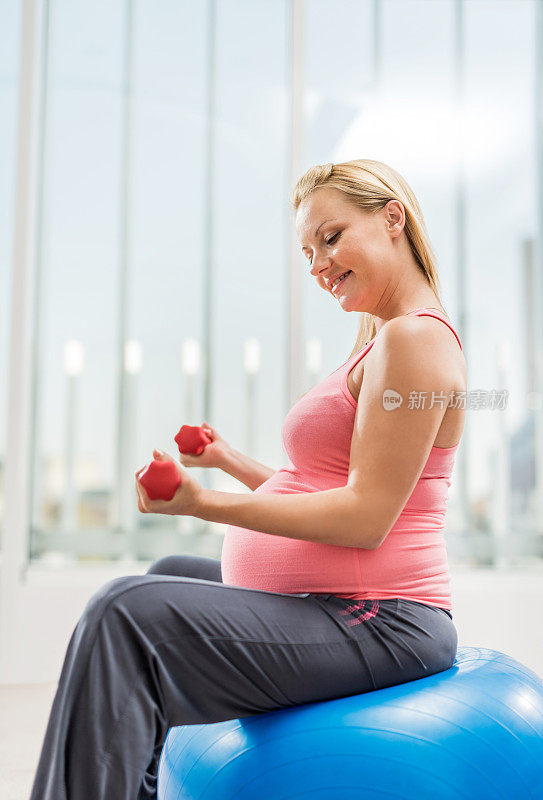 孕妇在健身球上用哑铃锻炼。