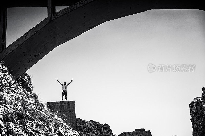 一个人在桥下的岩石上举起手臂