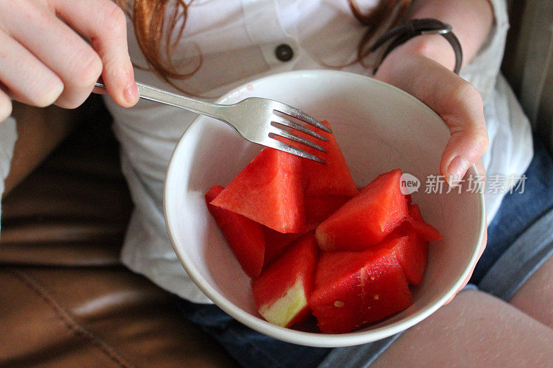 女孩在沙发上吃健康零食的形象，切成小块的西瓜