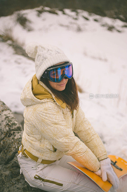 女人拿着滑雪板，背景是高山