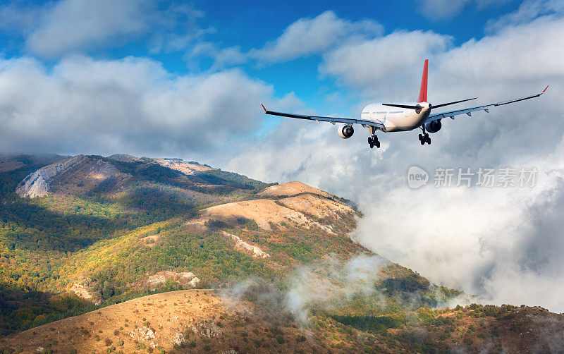 飞机。日落时分，白色的客机飞过群山、绿林和白云。的旅程。客机正在降落。商务旅行。商用飞机