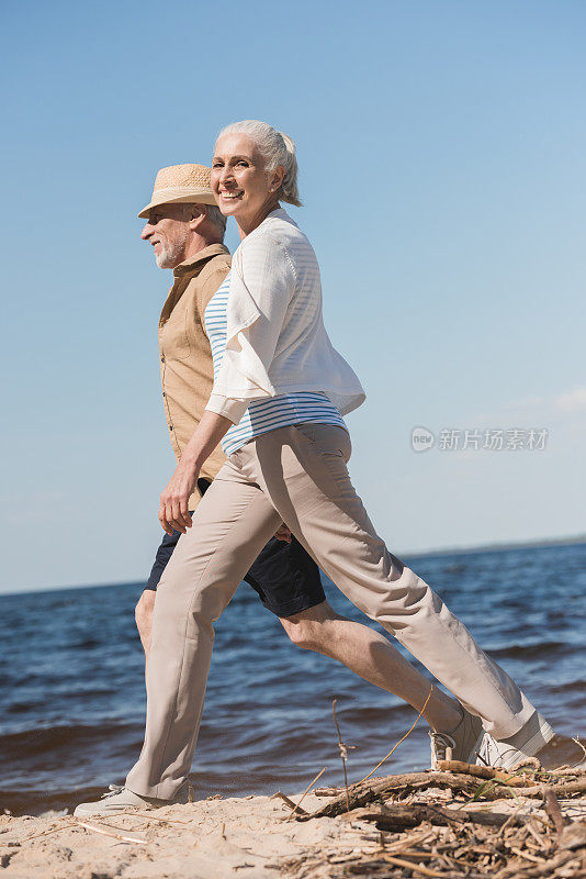 侧视图，幸福的老年夫妇手牵着手走在沙滩上