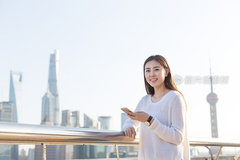 年轻美丽的亚洲女人在现代城市玩手机