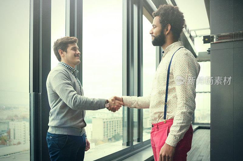 两个年轻的商人在现代化的办公大厅里握手。