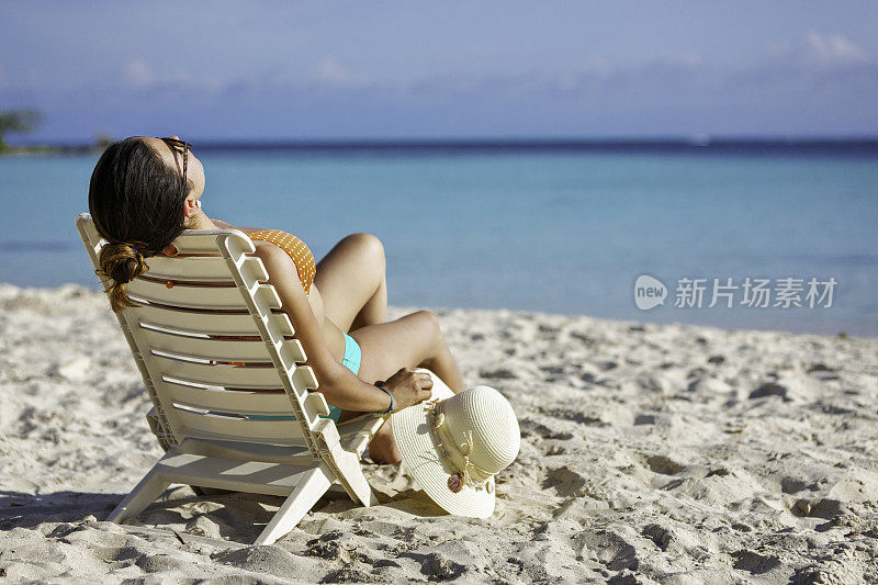 年轻女子日光浴和放松在椅子上的热带白沙岛海滩在加勒比海