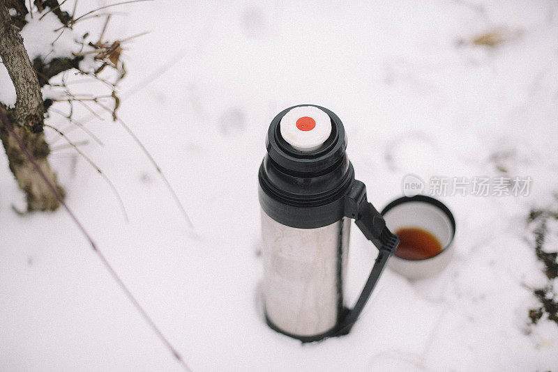 在冬天的森林背景上，女人用手从保温瓶里倒出热茶或咖啡。