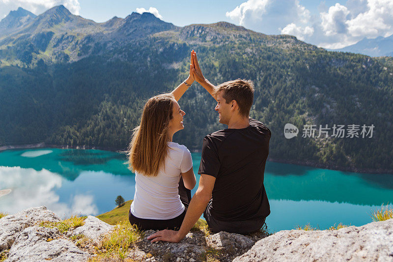 一对相爱的年轻夫妇在一个美丽的全景为背景的岩石上击掌。瑞士阿尔卑斯山