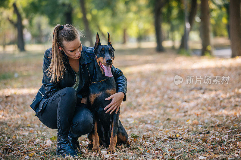 一个女人在公园里拥抱杜宾犬
