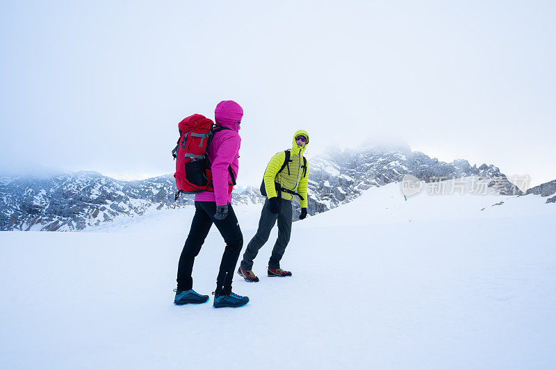 登山运动员夫妇在寒冷的暴风雪天在山上徒步旅行