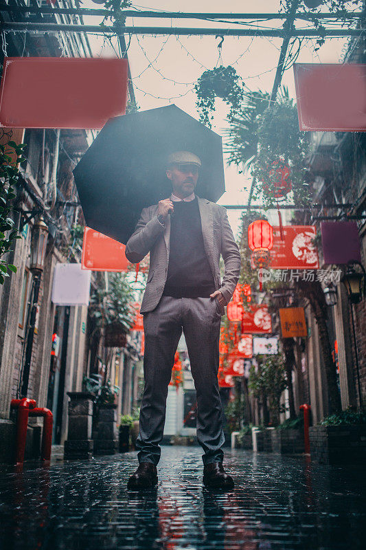 在中国城的街道上打着伞的现代绅士