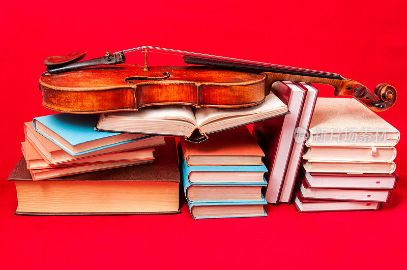 一堆书和一把旧小提琴放在不同的位置