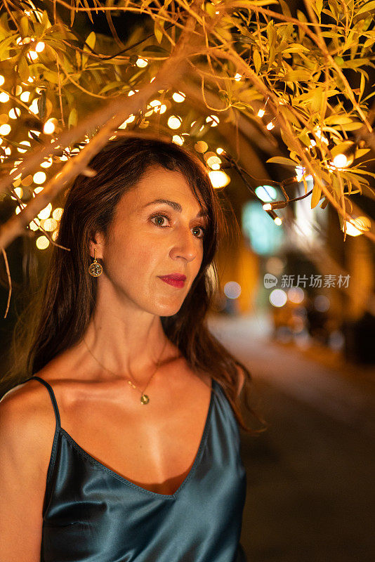 在巴塞罗那的街道上，一个优雅的女人在装饰灯光下