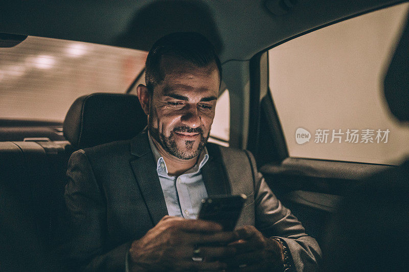 现代人坐在汽车后座上，用着智能手机