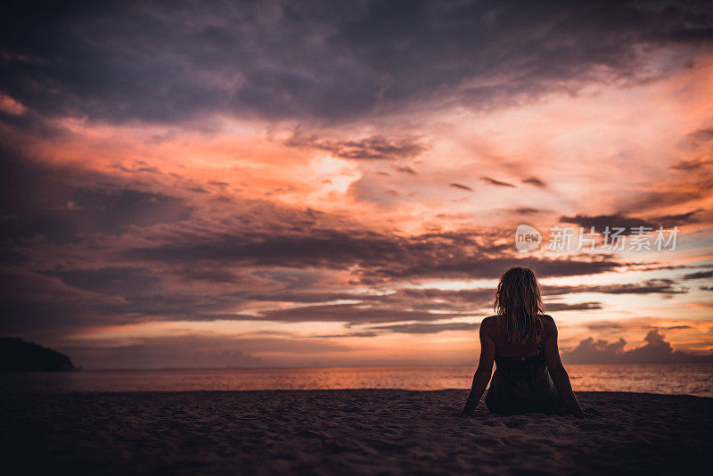 日落时在海滩上放松的女人的后视图。