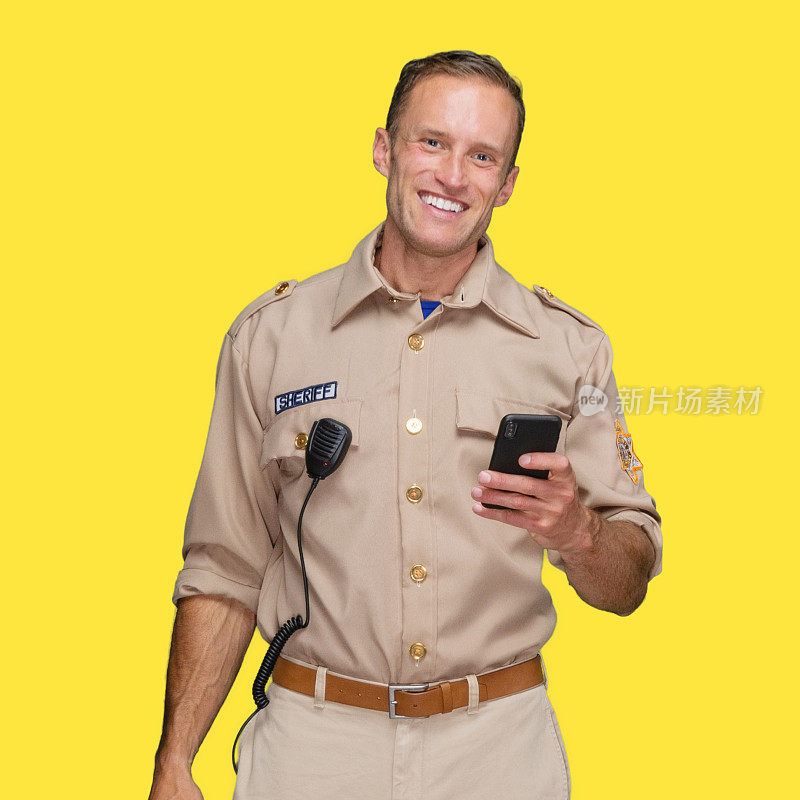 白人男性警察站在黄色背景下佩戴警徽并使用智能手机