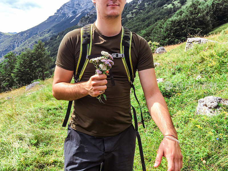 年轻的徒步旅行者在草地上采集鲜花