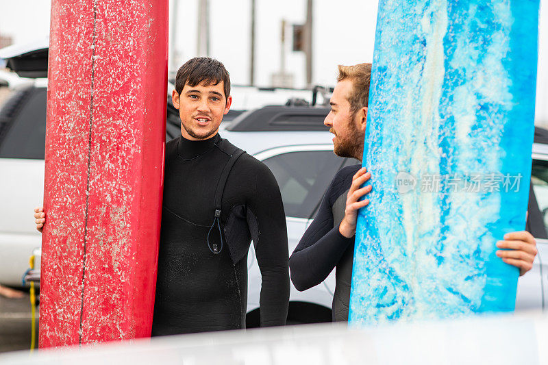 两个冲浪者站着说话，并拿着冲浪板