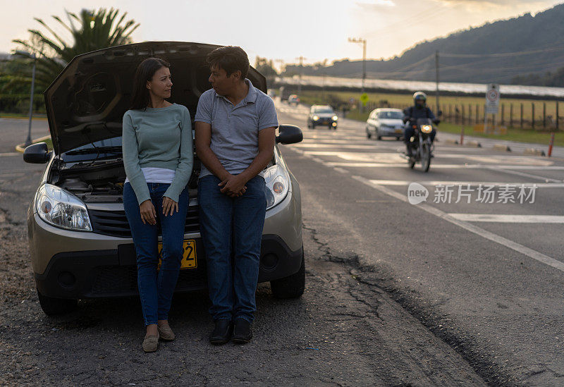 一对夫妇靠在需要路边援助的车辆的引擎盖上