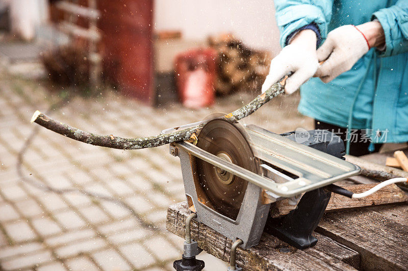 戴着手套的人在电锯上手工锯木头。