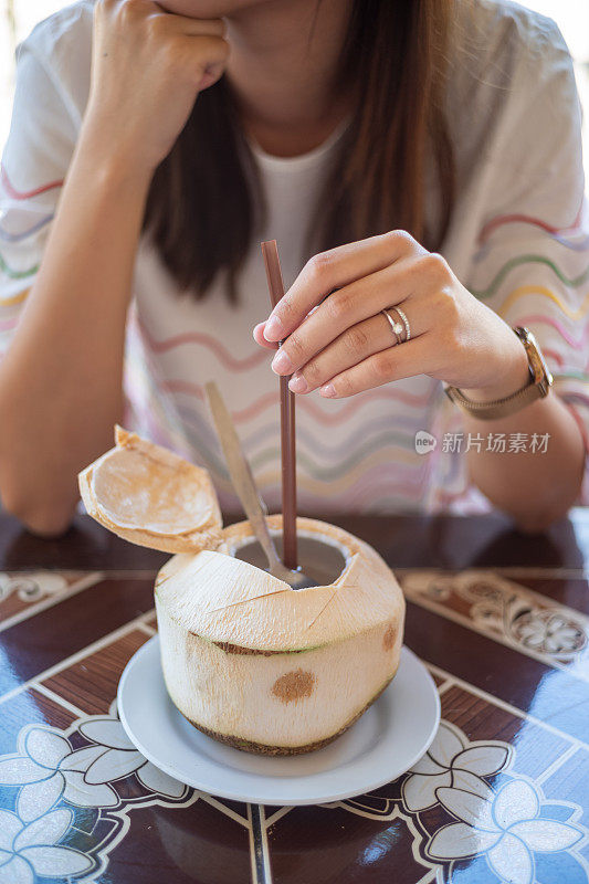 年轻的亚洲女人享受椰子汁在餐厅