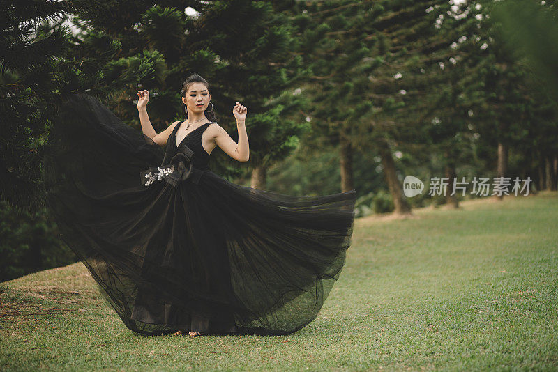 年轻的亚洲华人新娘穿着黑色婚纱在公园摆姿势