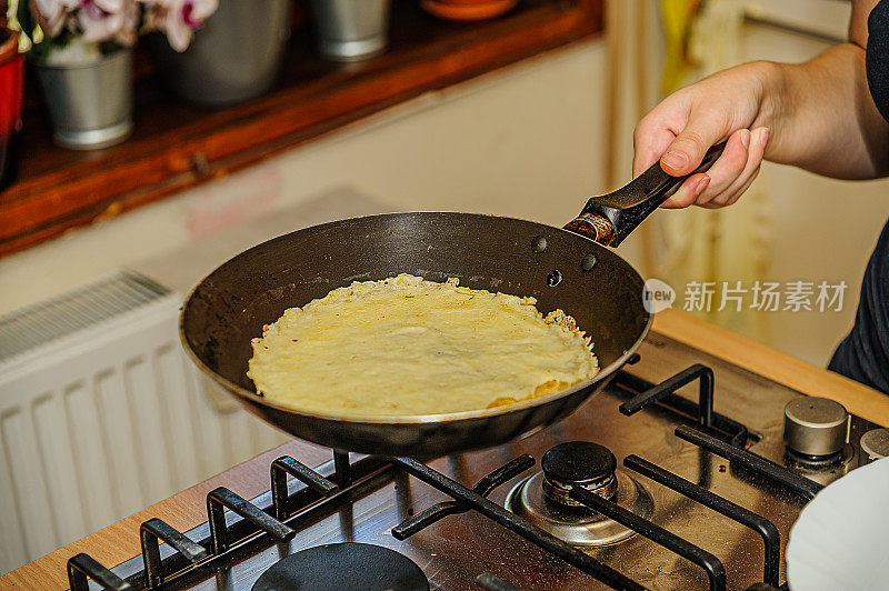 一名女厨师正在用一个油煎锅在家做煎饼。