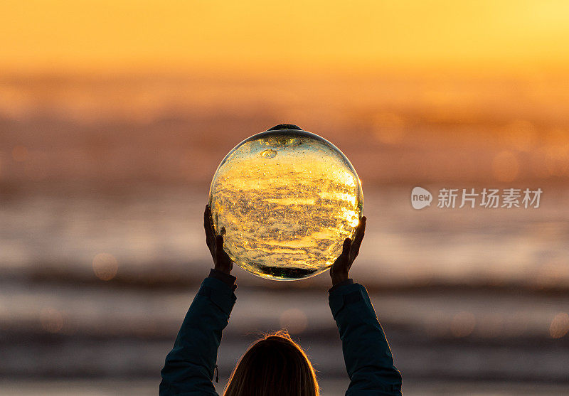 日出时，女人在海滩边拿着水晶球