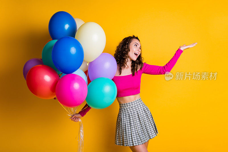 肖像照片的快乐女学生拿着气球微笑保持手孤立在明亮的黄色背景