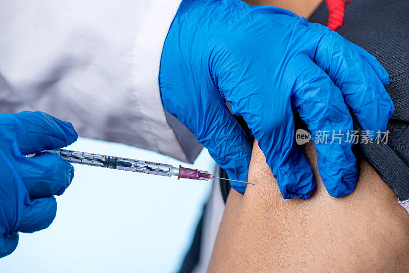 医生或护士的手在蓝色医疗手套注射一针疫苗到一个男人病人。