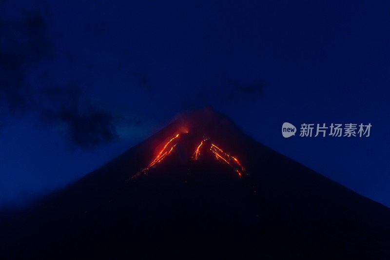 活火山喷发夜景，炽热的红色熔岩流从火山口喷发，蓝色的天空在黄昏。山地旅游景观背景